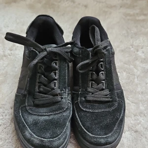 Svarta sneakers från Polo - Snygga svarta sneakers från Polo i mocka och syntetmaterial. Skorna har klassisk snörning och en diskret logga på hälen. Perfekta för en stilren look.