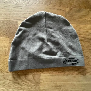 Grå mössa från Starlight - Snygg grå mössa från Starlight med broderad logga framtill. Perfekt för att hålla värmen under kyliga dagar. Enkel och stilren design som passar till det mesta.