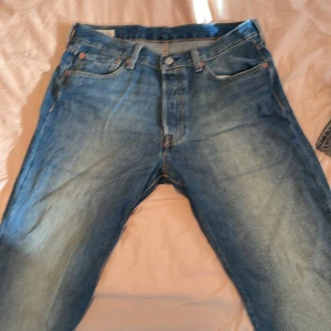 Blå jeans från Levi's - Säljer ett par klassiska blå jeans från Levi's med fem fickor och knappgylf. De har en traditionell passform och är perfekta för en avslappnad stil. Levi's-loggan syns tydligt på baksidan. Använt två gånger 