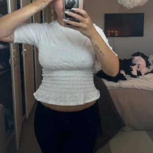 Vit ribbad topp - Säljer en söt vit ribbad topp med korta ärmar och volangdetalj i nederkant. Toppen har en tight passform och är perfekt för en stilren look. Passar bra till både jeans och kjol. Fläck på tröjan ( se sista bild) Hör av dig vid intresse! 🤍