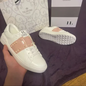 Valentino Garavani Rockstud sneakers - Snygga vita Valentino Garavani Rockstud sneakers med rosa detaljer och ikoniska nitar. Har använt dem en gång sen jag köpte dem och dem är lite smutsigare under sulan och lite på snöret . . Nypris runt 8000 köpte dem för 7000 men dem var lite små på mig. Box och påse är de som medföljer, som visas på första bilden. Storleken har suddats ut. 