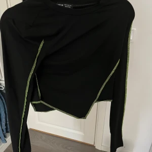 Svart långärmad topp från Shein - Snygg svart långärmad topp från Shein med kontrasterande gröna sömmar. Toppen har en asymmetrisk design och är perfekt för en trendig look.