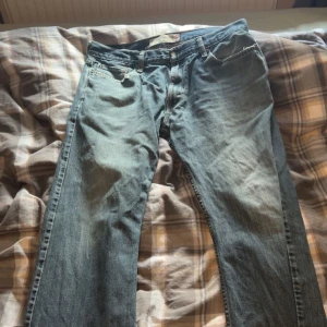 Blå jeansbyxor med fransar - Säljer ett par klassiska blå jeansbyxor med fransade kanter. De har en normal passform och är perfekta för en avslappnad stil. Byxorna har en traditionell femficksdesign och knappgylf.