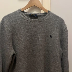 Grå stickad tröja från Polo Ralph Lauren - Säljer en stilren grå stickad tröja från Polo Ralph Lauren med rund halsringning och det klassiska logotypbroderiet på bröstet. Perfekt för en avslappnad och snygg look. Passar bra till både jeans och chinos. Tröjan är i storlek M och har använts fåtal gånger 