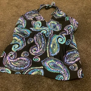 Mönstrad halterneck topp från Venus - Säljer en färgglad halterneck topp från Venus med ett livligt paisleymönster i blått, lila och grönt på svart bakgrund. Toppen har en knytning i nacken och en lätt v-ringad design. Perfekt för en somrig look! 🌸