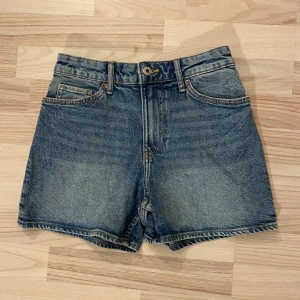 Blå jeansshorts från H&M - Snygga blå jeansshorts från H&M med klassisk femficksdesign och knappgylf. Perfekta för en avslappnad stil.