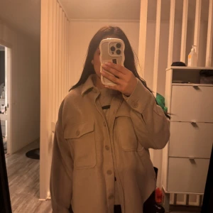 Beige overshirt - Säljer en stilren beige overshirt med knappar framtill och två stora bröstfickor. Perfekt för lager-på-lager-stil och passar bra till både vardag och mer avslappnade tillfällen. Från ginatricot i storlek S. Använd fåtal gånger