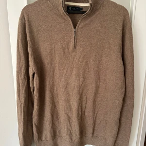 Beige tröja med dragkedja från Riley - Säljer en stilren beige tröja från Riley med dragkedja vid halsen. Tröjan har långa ärmar och en ribbad krage. 