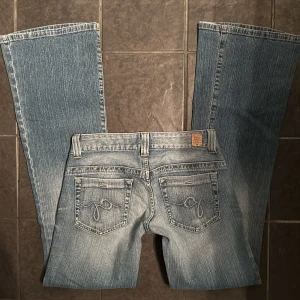 Lågmidjade utsvängda jeans  - Ursnygga lågmidjade utsvängda jeans från Guess med en klassisk femficksdesign och subtila slitningar. Midjemått tvärsöver: 34 cm. Innerbenslängd: 81 cm. 