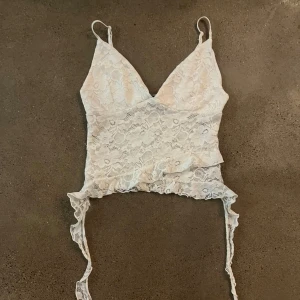 Vit spetslinne med smala axelband - Säljer ett vackert vitt spetslinne med smala axelband och v-ringning. Toppen är croppad och köpt i Italien. Perfekt för sommaren och varma utekvällar!