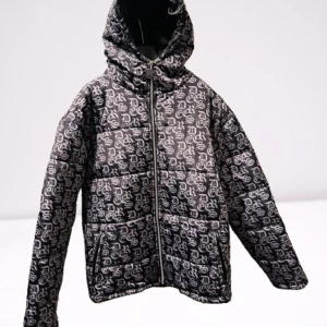 Svart mönstrad pufferjacka från Decrese - Snygg svart pufferjacka från Decrese med ett unikt vitt mönster. Jackan har en dragkedja framtill och en praktisk huva. Perfekt för kyligare dagar  den här jackan finns bara en så den är unik ingen har den modellen . 