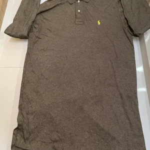 Brun långärmad tröja Polo Ralph Lauren - Brun långärmad tröja från Polo Ralph Lauren i mjuk bomull.Ny pris 1199kr. Klassisk pikékrage med knappar framtill och ikonisk gul broderad logga på bröstet. Perfekt för en chill och stilren look.