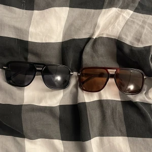 Två retro solglasögon i svart och brunt - Säljer två par solglasögon med cool retrostil. Ena paret har svart båge och mörka glas, det andra har brunröd båge och bruna glas. Båda har en klassisk pilotform och metalliga detaljer vid skalmarna. Perfekta för att lyfta din stil i sommar.