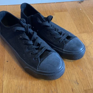 Svarta sneakers från Kappa - Heltsvarta sneakers från Kappa med klassisk låg profil och rund tå. Skorna har ovandel i canvas, svart gummisula och snörning framtill. Kappa-loggan syns broderad på hälen. Perfekta för en clean och stilren look.