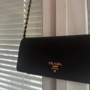 Svart kuvertväska i skinn från Prada - Säljer en så snygg svart kuvertväska från Prada i äkta skinn med guldfärgad kedjerem. Äkthetsbevis finns vid intresse så hör av er!
