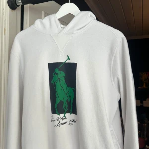 Vit hoodie från Polo Ralph Lauren - Vit hoodie från Polo Ralph Lauren med ett stort tryck på framsidan. Inga defekter. Skriv om du har frågor eller prisförslag🙌🏽