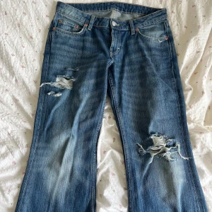Blå bootcut jeans från Weekday - Snygga blå jeans från Weekday med bootcut passform och slitna detaljer på både fram- och baksida. Jeansen har klassisk femficksdesign, normal midja och är gjorda i jeansmaterial. Perfekta för en avslappnad och trendig look.