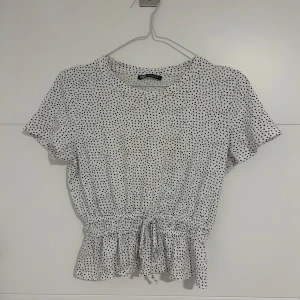 Vit prickig blus med knyt i midjan - Säljer en söt vit blus med svarta prickar och korta ärmar. Blusen har resår och knytband midjan!🥰🥰 pris är pga att den är efterfrågad och svår att få tag på❤️❤️