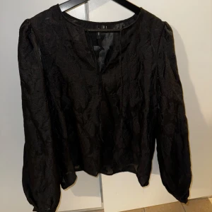 Svart blommig blus från Vero Moda - Säljer en svart blus från Vero Moda med subtilt blommönster i tyget. Blusen har långärmade puffärmar och en lätt v-ringning framtill. Tunt, lätt material som ger en luftig känsla och snygg struktur. Perfekt att styla med jeans eller kjol.