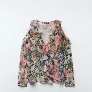 Blommig volangblus från Zara - Superfin blommig blus från Zara med volangdetaljer och v-ringning. Långärmad modell i tunn, luftig polyester med öppna axlar och romantiskt mönster i rosa, beige, grön och lila toner. Perfekt för dig som gillar färg och statement-plagg!