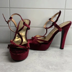 Vinröda sammetsklackar med platå - Snygga vinröda sandaler med hög klack och platåsula i mjuk sammet. Skorna har smala remmar med knyt runt vristen och öppen tå. Insidan är guldfärgad för extra lyxig känsla. Perfekta för dig som vill sticka ut.