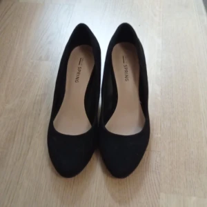Svarta pumps från Call It Spring st 35 - Stilrena svarta pumps från Call It Spring med rund tå och låg klack i metallfinish. Skorna är i mockaimitation och har en klassisk siluett som passar till många olika looks. Perfekta för dig som gillar en enkel men elegant stil. storlek 35. innermått :22.5cm, köpte de här på plick, trodde det skulle passa men tyvärr inte 
