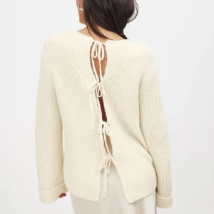 Vit stickad tröja med snörning bak - Superfin off white stickad tröja med unika snörningsdetaljer längs ryggen. Tröjan har lång ärm, rund halsringning och en mjuk, ribbad struktur. Perfekt för dig som vill ha något stilrent men ändå med en twist.