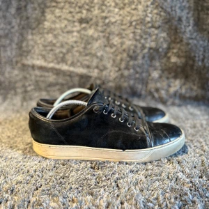Lanvin skor  - Svarta sneakers med ovandel i mocka och tåparti i skinn. Skorna har svarta snören, silverfärgade öljetter och en beige platt sula. Klassisk rund tå och stilren design som passar till det mesta.