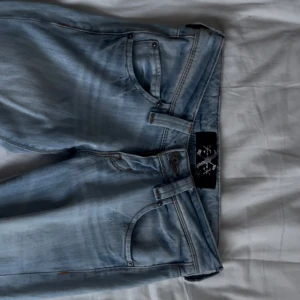 Ljusblå bootcut jeans med låg midja -  Ljusblå jeans med snygg bootcut-modell och låg midja. Jeansen har klassisk femficksdesign, slitningar vid benslut och är tillverkade i mjukt denimtyg. Perfekta för dig som gillar en avslappnad och trendig look. Har en liten defekt bak på jeansen (bild finns) men inget man tänker på. Står att jeansen är i storlek W26 L31!