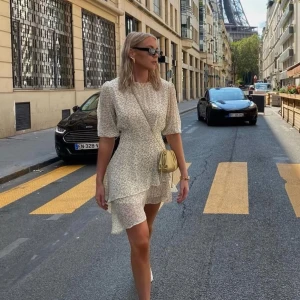 Blommig kortklänning från Adoore - Superfin kortklänning från Adoore i ljus bas med små gula blommor. Klänningen har volangdetaljer, trekvartsärm och dragkedja i ryggen. Perfekt för sommarens alla tillfällen. 