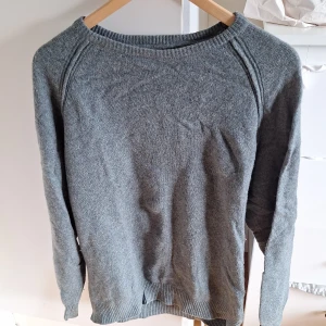 Grå/grön stickad tröja från Dressmann - En enkel och stilren grå stickad tröja från Dressmann i storlek L. Tröjan har rund halsringning, ribbade muddar och är långärmad. Perfekt för lager-på-lager och funkar till många olika outfits.