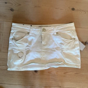 Vit jeansminikjol med slitningar - Lågmidjade vit jeanskjol med slitningar. Midjemått rakt över: 37,5cm. Hör av er vid fler frågor💕