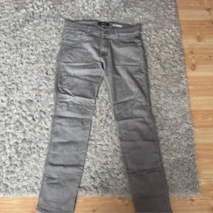 Grå Replay Anbass jeans straight fit - Säljer ett par gråa Replay Anbass jeans med klassisk femficksdesign och snygga detaljer på bakfickorna. Jeansen har rak passform och är tillverkade i mjukt denimtyg. Perfekta för dig som gillar stilrena och bekväma jeans.
