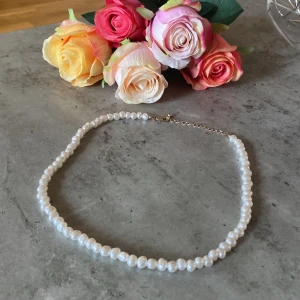 Klassiskt pärlhalsband med guldlås - Ett stilrent halsband med vita oregelbundna pärlor och ett tunt guldfärgat lås. Perfekt för dig som gillar en tidlös och elegant look. Pärlorna har en naturlig glans och halsbandet är lätt att matcha med andra smycken.