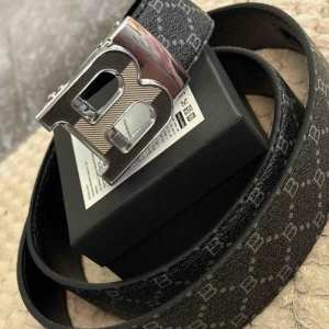 Svart Balmain bälte med B-spänne - Snyggt svart bälte från Balmain med silverfärgat B-spänne. Bältet har ett diskret mönster med små B-loggor över hela remmen och är gjort i skinn. Perfekt accessoar för att lyfta din outfit.