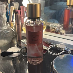 Victoria's Secret Romantic mist - Victoria's Secret Romantic är en body mist i en genomskinlig plastflaska med rosa toner och guldig kork. Doften har inslag av rosa blomblad och mjuk mysk, perfekt för dig som gillar fräscha och blommiga parfymer. Flaskan rymmer 250 ml och har en stilren, feminin design.