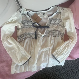 Vit Odd Molly blus - Supersöt vit blus från Odd Molly med broderade detaljer i blått och beige och även blå knutbar rosett. Köpt på Sellpy i bra skick men aldrig använd av mig, ser helt ny ut💗
