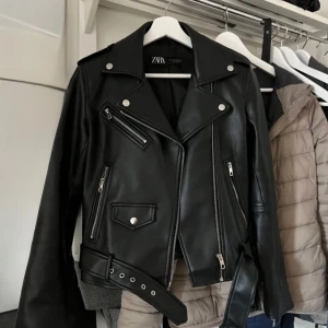 Svart skinnjacka från Zara - Snygg svart skinnjacka från Zara med dragkedja och knappar. Har storleken S och Xs. PRIS KAN DISKUTERAS!!!