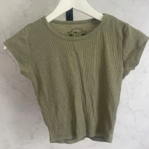 Olivgrön ribbad topp - Snygg olivgrön ribbad topp. Modellen är croppad med korta ärmar och rund halsringning. Perfekt för dig som gillar en enkel men trendig stil. Tunt och mjukt material som känns skönt mot huden.