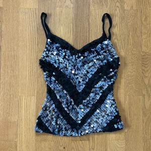 Glittrig paljettopp från Nutshell - Supersnygg glittrig topp från Nutshell med svarta och silvriga paljetter i ett V-format mönster. Perfekt till en varm sommardag eller fest!