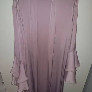 Ljuslila två delars abaya  - Superfin abaya i ljuslila med volangärmar och glittriga paljettkanter. Klänningen har en rak passform och har en inre och yttre del. Helt oanvänd, 115 cm bust mått 