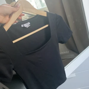 Svart croppad topp från Amisu - Svart croppad topp från Amisu med fyrkantig urringning och korta ärmar. Enkel och stilren design i mjuk bomull, perfekt att matcha med höga jeans eller kjol. Snygg basic som funkar året runt.