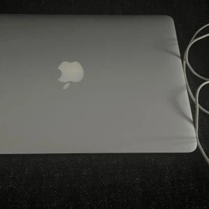 MacBook  - Bilderna visar en MacBook Air-laptop från Apple, inte en bok. Produkten har en stilren design, bakgrundsbelyst tangentbord och kör macOS. Perfekt för studier, kreativt arbete eller underhållning. Laddare medföljer.