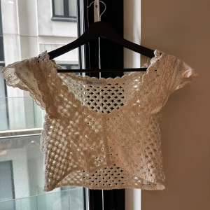Vit virkad croppad topp från Zara - Superfin croppad topp från Zara i vit virkad bomull med korta ärmar och v-ringning. Toppen har ett luftigt, genombrutet mönster och romantiska spetsdetaljer på ärmarna. Perfekt för varma dagar och snygg att styla lager på lager.