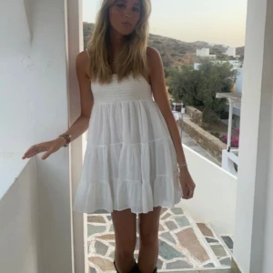 Vit kort sommarklänning från Zara - Supersöt vit kort klänning från Zara med smock upptill och volangig kjol. Ärmlös modell med tunna axelband och luftig passform, perfekt för varma dagar. Lätt och flowy känsla som ger en chill vibe.