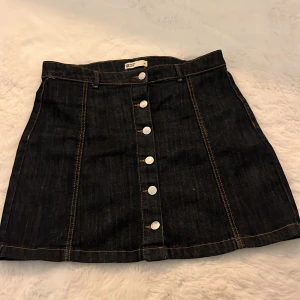 Svart jeanskjol med knappar - Mörk jeanskjol från G perfect jeans ,med snygga silvriga knappar framtill och kontrastsömmar. Kjolen är kort och har bälteshällor i midjan. Aldrig använd.