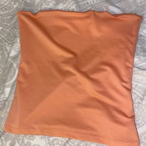 Orange bandeau tubtopp - Säljer en enkel och snygg orange bandeau tubtopp. Toppen är ärmlös och har en slät, figurnära passform som sitter perfekt på plats. Perfekt för varma dagar eller när du vill ha en clean look. Superenkel att matcha med jeans eller kjol.