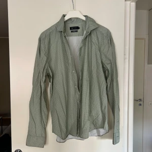 Grön mönstrad skjorta från Riley - Snygg grön skjorta från Riley med diskret geometriskt mönster. Skjortan har lång ärm, klassisk krage och knäppning framtill. Slim fit-modell som sitter tajt och stilrent. Perfekt för dig som gillar en fräsch och modern look. Nypris 1100kr
