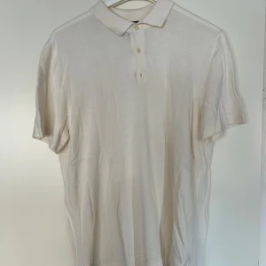 Beige pikétröja från H&M Slim Fit - Snygg beige pikétröja från H&M i slim fit-modell. Tröjan har klassisk krage, korta ärmar och knäppning med två knappar framtill. Perfekt för en clean och stilren look. Tillverkad i mjukt material som känns skönt mot huden.