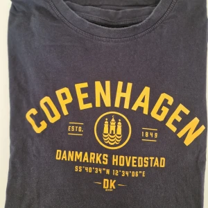 Navy t-shirt Copenhagen print - Cool navy t-shirt med gult Copenhagen-tryck och text om Danmarks huvudstad. Mjuk och skön i bomull, perfekt för dig som gillar streetstyle och grafiska prints.